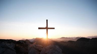 Une croix (crucifix) au sommet d’une chaîne de montagnes en silhouettes sur fond de de soleil levant.
