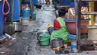 Uma senhora agachada, lavando pratos em uma ruela na Índia