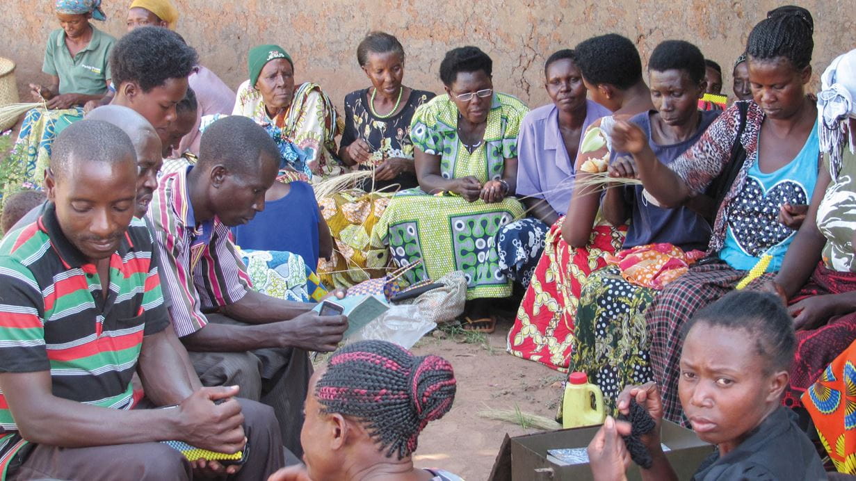 Homens e mulheres de um grupo de autoajuda em Uganda sentados no chão amarrando feno como parte de uma iniciativa de poupança e investimento em pequenas empresas