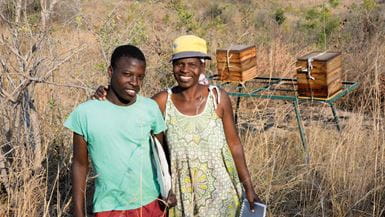 Une Africaine et son fils se tiennent devant leurs ruches dans une terre forestière sèche.