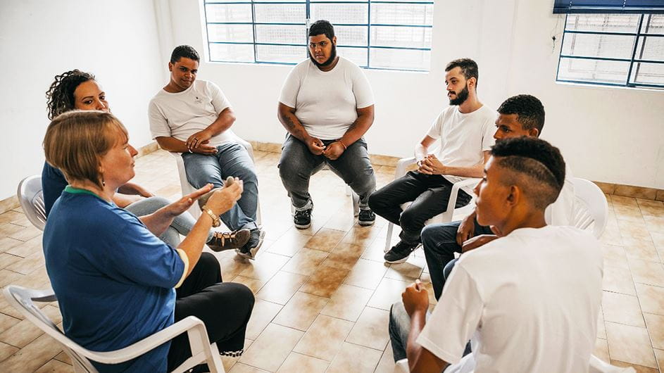 Jovens em uma prisão no Brasil sentados em círculo e conversando com uma mulher que está oferecendo apoio a eles