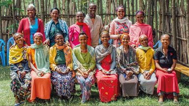 A group of brightly clothed, smiling women and one man pose for a photo in a rural village setting in Ethiopia