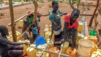 Un grupo de mujeres y niños utilizan recipientes de plástico amarillos para recoger agua de los grifos en Uganda