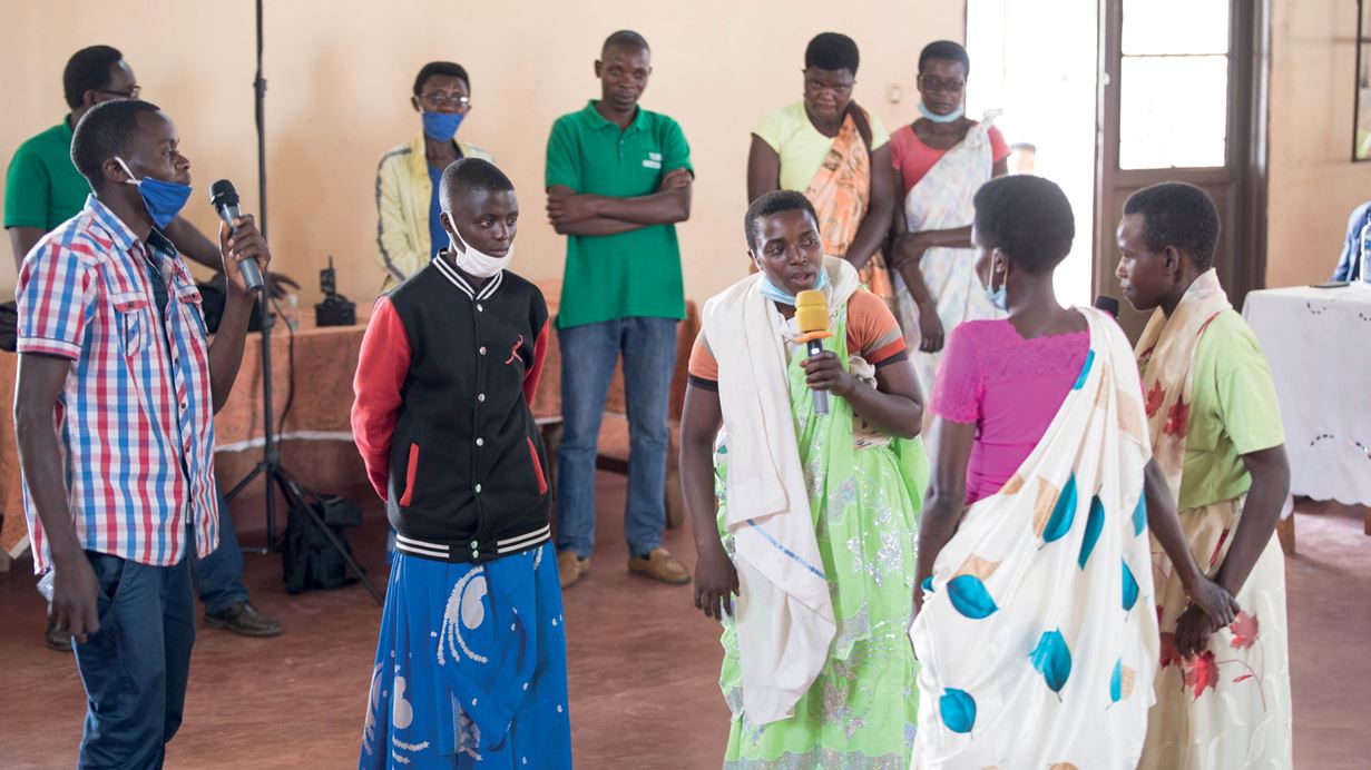 Un grupo de personas, de pie en una sala, hablan por los micrófonos como parte de un taller de teatro en el Día de la Paz en Burundi