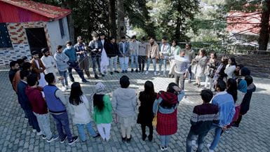 Um grande grupo de homens e mulheres paquistaneses de diferentes religiões, em um círculo, segurando pedaços de barbante cruzados para ilustrar a construção da paz