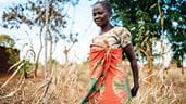 Uma mulher, usando um vestido estampado vermelho e laranja, caminhando por um campo perto de seu povoado, na Tanzânia