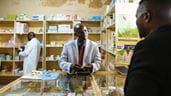 Un pharmacien se tient au comptoir de l’hôpital municipal de Bailundo, en Angola, et sert un client.