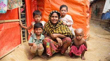 Uma mãe e seus quatro filhos pequenos ajoelhados do lado de fora de sua barraca em Bangladesh