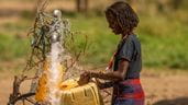 Uma moradora local etíope enchendo sua bombona de plástico com água fresca saindo de uma torneira