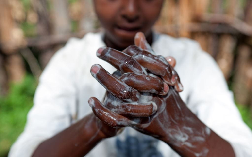 Un jeune garçon montre comment se laver les mains en faisant mousser du savon.