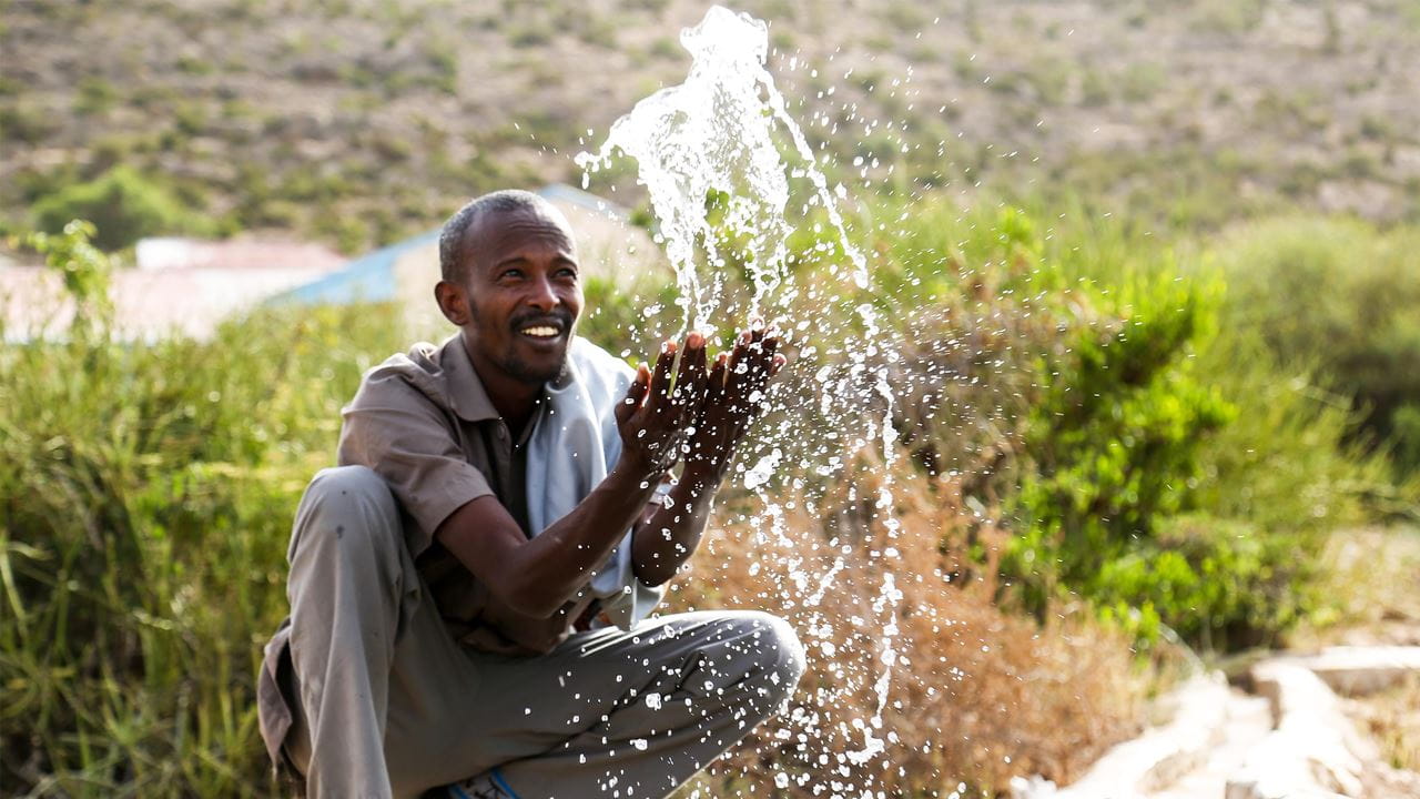 Um homem respingando água em um ponto de água recém construído, usado para irrigação no povoado de Cala culle, na Somália. Foto: Colin Cosier/Tearfund