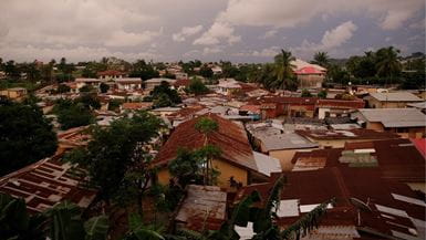 Overhead view of a dense village with rusty rooftops under a cloudy, grey sky.