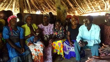 Group of African adults and a child seated together under a thatched roof.