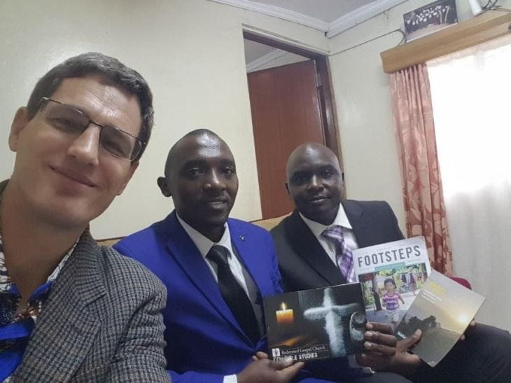 El autor del artículo y dos hombres de Nigeria sonríen a la cámara y muestran materiales de Tearfund, incluyendo una copia de la revista Paso a Paso.