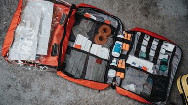 Um kit de primeiros socorros grande aberto, mostrando três compartimentos contendo vários itens, como creme anti-séptico, curativos adesivos e bandagens
