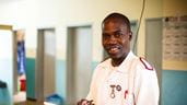 Um agente de saúde malawiano vestindo seu uniforme branco e vermelho e sorrindo para a câmera enquanto toma notas