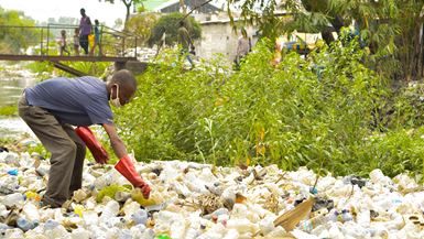Un homme équipé de gants en caoutchouc rouge trie une pile de bouteilles en plastique jetées à Kinshasa, en RDC.
