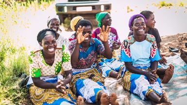 Sept femmes d’un groupe d’entraide au Malawi assises sur une natte à même le sol rient en attendant une réunion.
