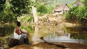 Un hombre sentado sobre el borde de un viejo bote pesquero de metal mira al otro lado del río en una zona rural de Honduras