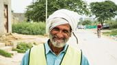 Un homme se tient dans une rue poussiéreuse du Pakistan ; il porte un turban et un gilet jaune.
