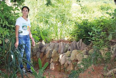 Una mujer llamada María, con camiseta blanca, construye muros de piedras para contener el agua de lluvia