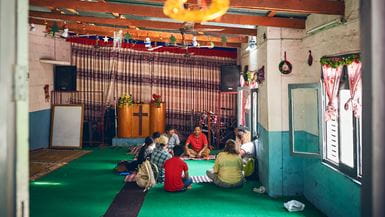 Um grupo de homens e mulheres sentados sobre um tapete verde no chão de uma igreja no Nepal, discutindo o processo de Mobilização de Igrejas e Comunidades (MIC)