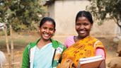 Deux femmes d’un groupe communautaire du Bangladesh sourient à la caméra, l’une d’elles tient un livre à la main.