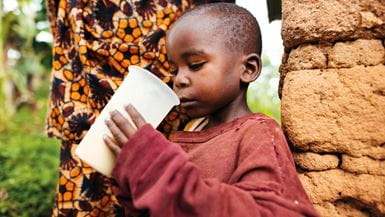 Un jeune garçon en pull rouge du nom d’Edouard déguste un porridge nutritif au Burundi.