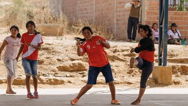 Quatro meninas vestindo camisas de futebol vermelhas, chutando uma bola e jogando futebol na Bolívia