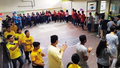 Un grupo de jóvenes de comunidades de alto riesgo de Guatemala, con camisetas amarillas, rojas, azules y grises, aplauden y se mueven en círculo como parte de un ejercicio de formación de equipos