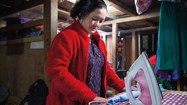 Dans son atelier de couture aux plafonds en poutres de bois, Shanti s’apprête à presser une chemise à col bleu, un fer à repasser à côté d’elle.