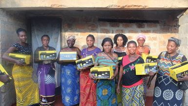 Neuf femmes d’un groupe d’entraide portent des boîtes en carton contenant des lampes qu’elles ont achetées grâce à un plan de paiement flexible.
