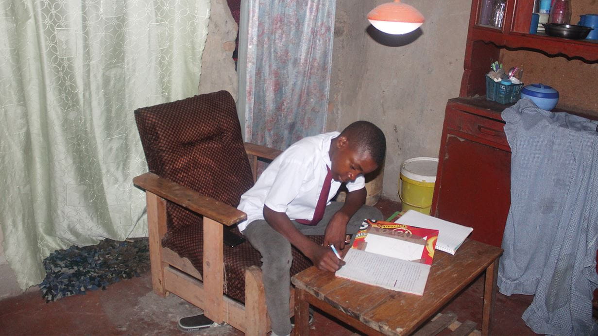 Um menino sentado em uma cadeira, vestido em seu uniforme escolar, terminando seus deveres de casa com a ajuda das lâmpadas de energia solar