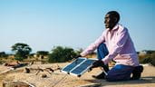 En Tanzanie, Lameck Chibago oriente un panneau solaire sur le toit de sa maison en direction du soleil.