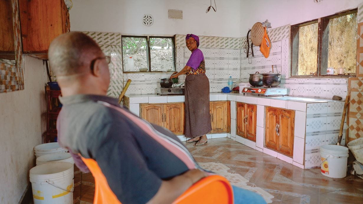 Marsha, junto al mueble de cocina, habla con su marido, que está sentado en un sillón