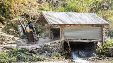 Una mujer llamada Phul Kumari lleva granos a un molino que funciona con el agua que sale de la pequeña planta de energía hidroeléctrica ubicada arriba del molino