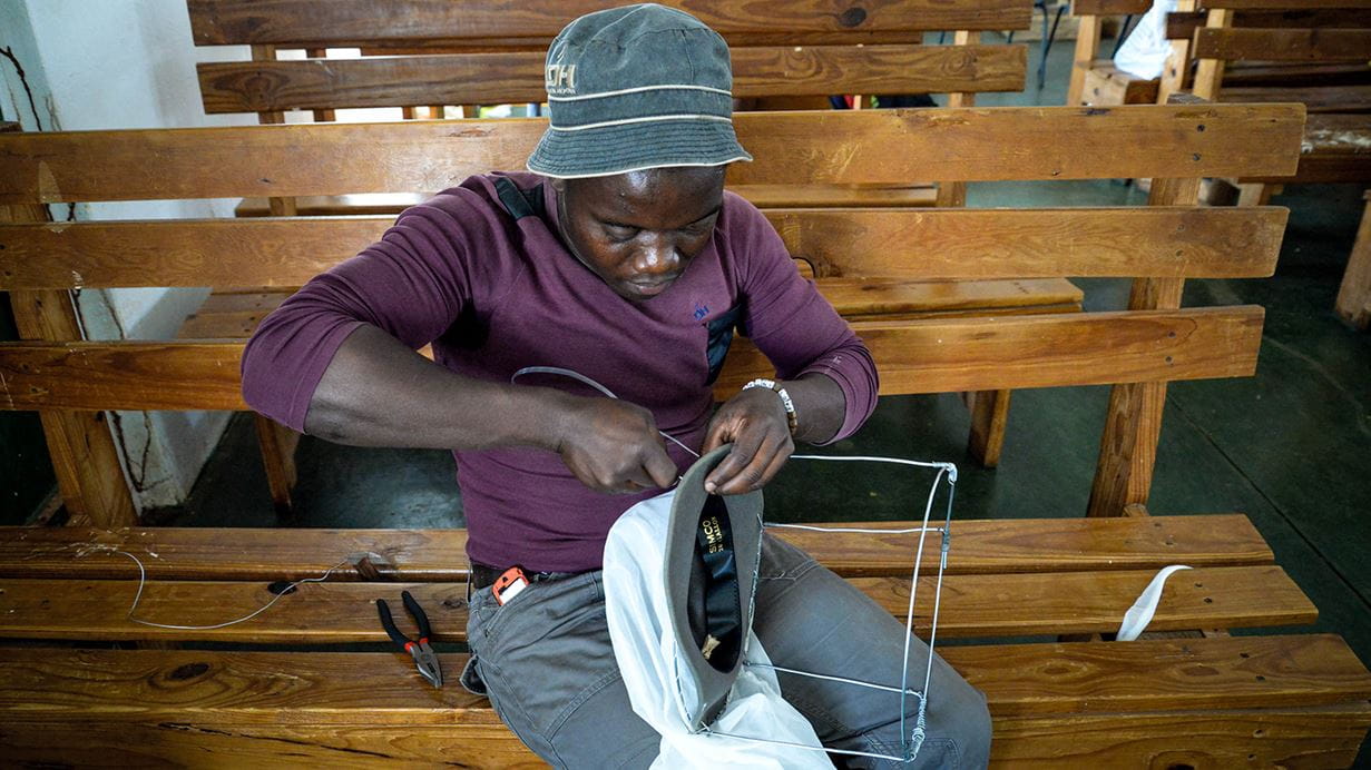 Un hombre con camiseta morada emplea una herramienta para fabricar equipos protectores contra colmenas
