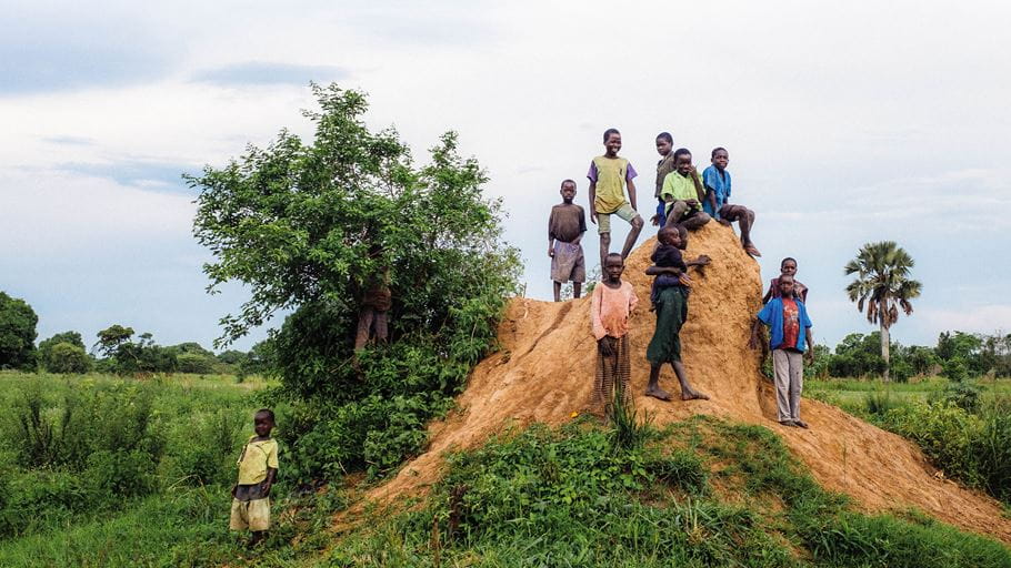 Des enfants se tiennent sur un grand monticule de terre fabriqué par des termites.