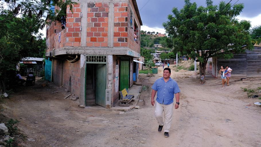 Un homme en chemise à col bleu clair marche sur le chemin poussiéreux d’un quartier en Colombie.