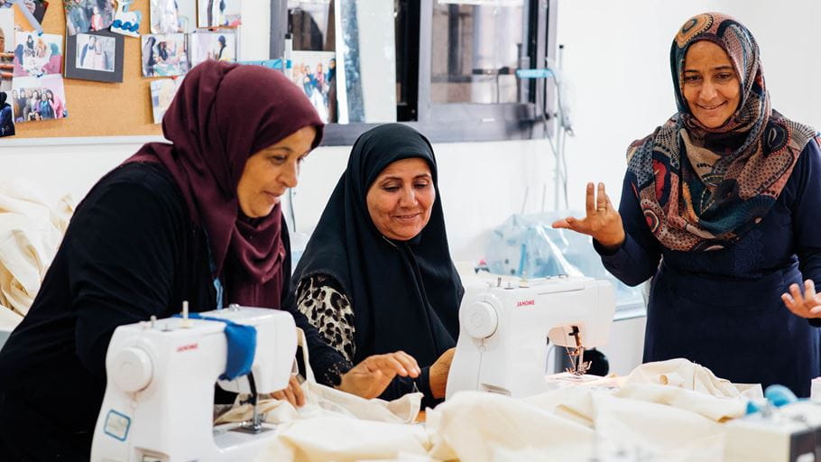 Trois femmes voilées du Moyen-Orient sont devant des machines à coudre pour apprendre à coudre.