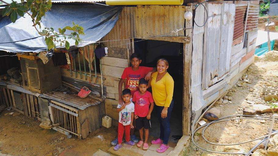 Geovanna y sus dos hijos posan a la entrada de su nuevo hogar, construido con láminas de zinc en Colombia