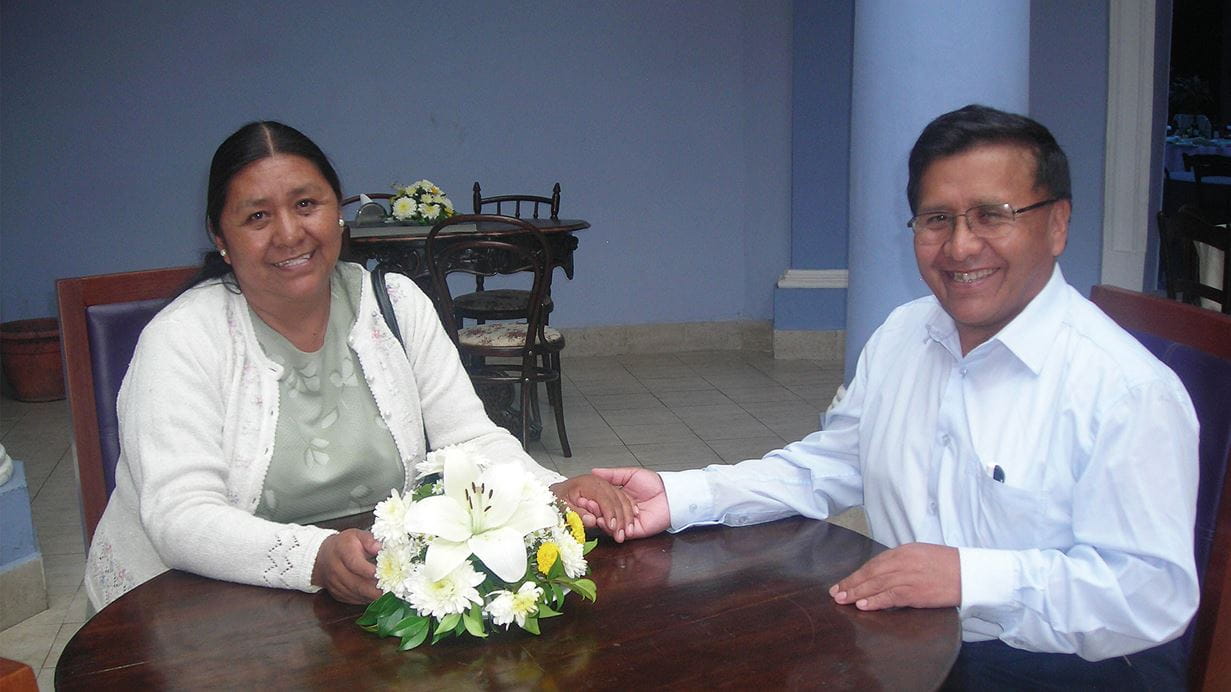 Ana, uma mulher boliviana, sentada à mesa e sorrindo para a câmera