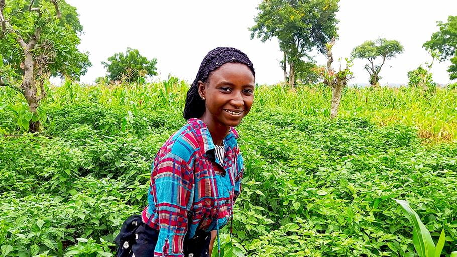 Uma mulher nigeriana sorrindo em frente às plantações que está cultivando 