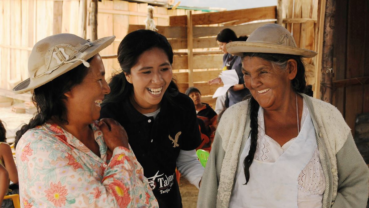Three Bolivian women smile and laugh together at a training workshop