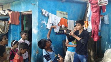 Um jovem na Índia usando seu telefone celular para filmar um grupo de crianças sorridentes