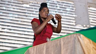 A young African woman with a handheld microphone delivering an impassioned speech