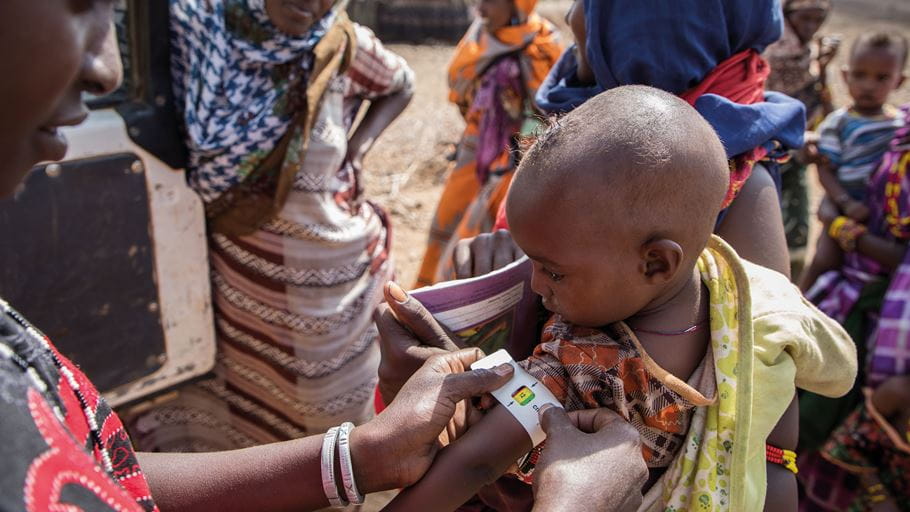 Una mujer de Kenia pone una cinta codificada por colores alrededor de la parte superior del brazo de un niño pequeño