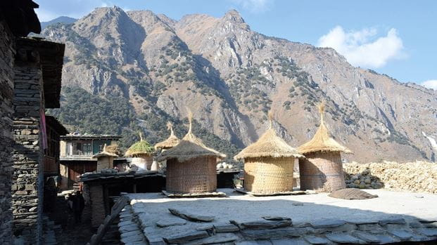 Plusieurs greniers à céréales en bambou avec des toits en paille pointus sont installés sur un toit, dans un paysage montagneux