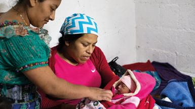 A female Guatemalan health promoter checks a newborn baby held by its mother
