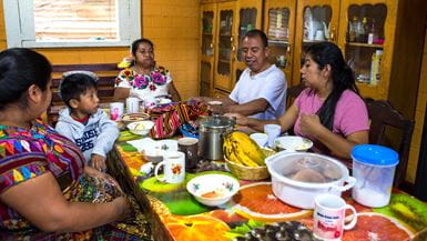 Uma família na Guatemala desfrutando uma refeição ao redor de uma mesa com uma toalha colorida